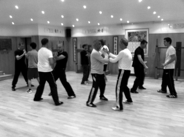 Gruppentraining in einem Raum, Teilnehmer üben Kampfsport miteinander.