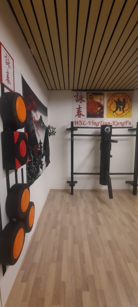 Trainingsraum mit Kampfsportgeräten und Wandkunst. Holzboden und helle Wände.
