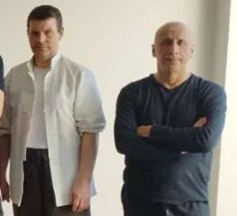 Zwei Männer stehen nebeneinander, einer in hellen und der andere in dunklen Kleidern.